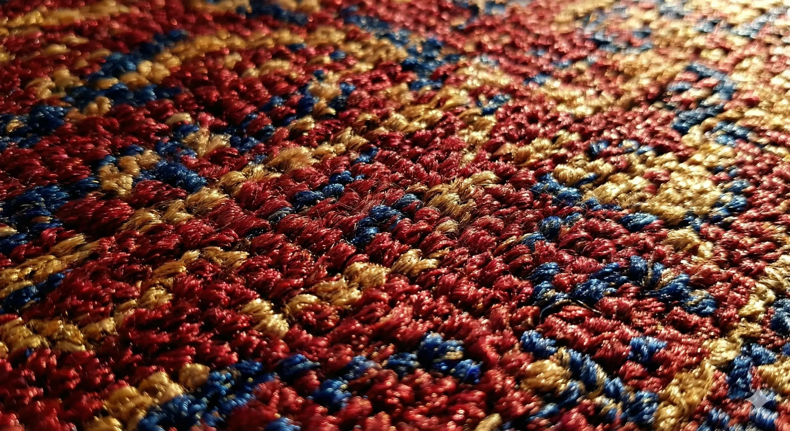 Photographie artistique en gros plan (macro) montrant la texture dense et soyeuse d'un tapis en soie de haute qualité après nettoyage. Une lumière rasante fait miroiter les fibres rouges, bleues et dorées, révélant la finesse des nœuds et la brillance retrouvée du tissage. L'image dégage une sensation de propreté et de luxe.