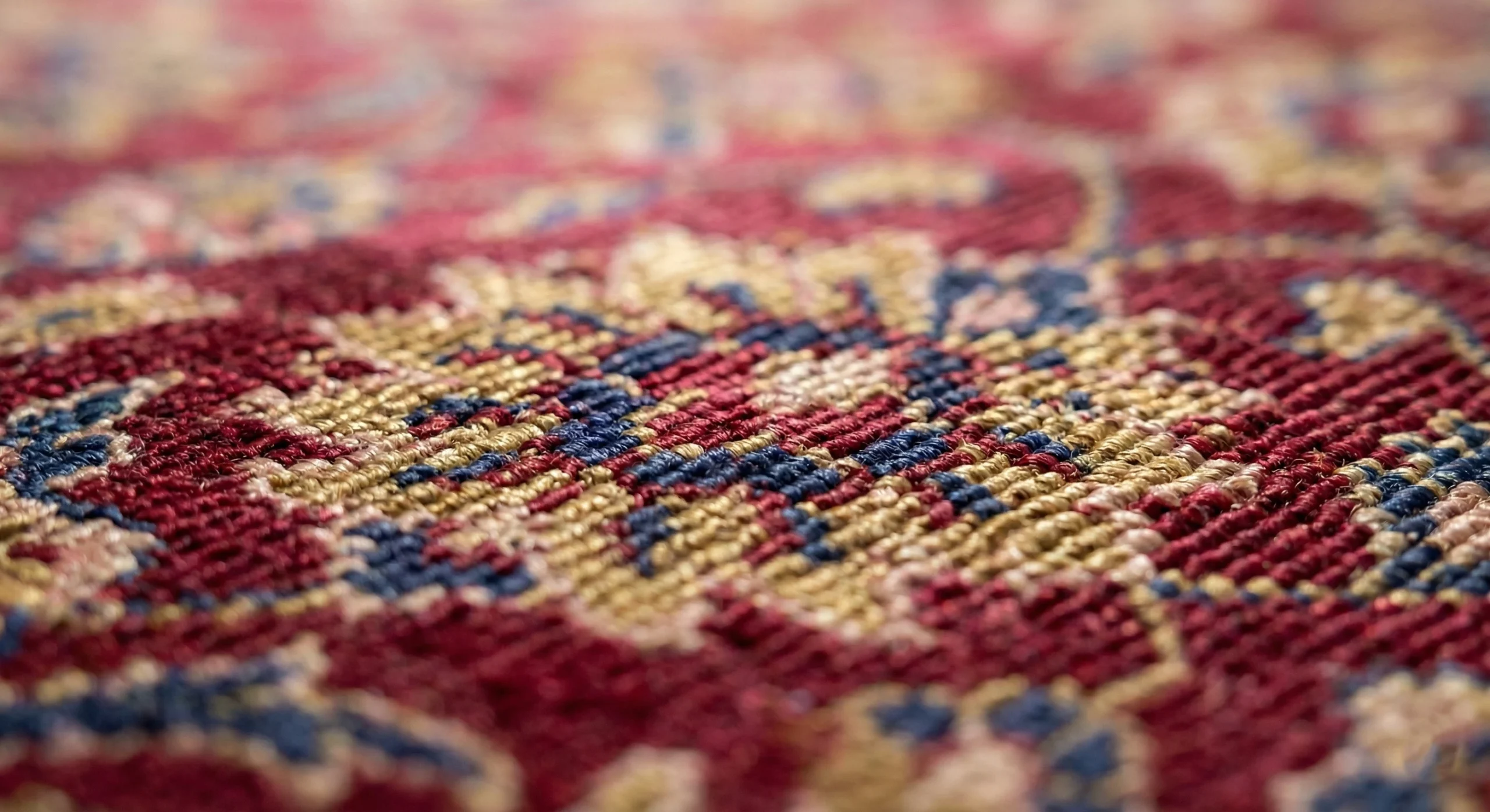 Gros plan détaillé sur les fibres finement tissées d'un authentique tapis persan aux riches motifs rouges, dorés et bleus, soulignant la délicatesse de ces matériaux nobles qui nécessitent un nettoyage expert.